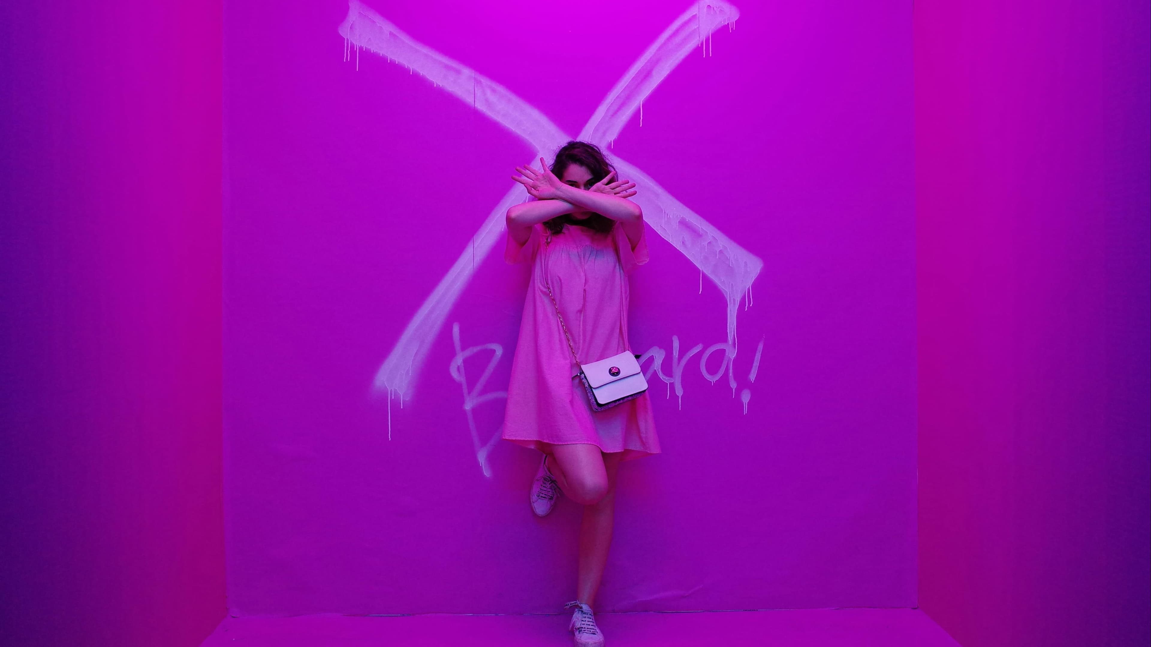 Person with arms outstretched wearing angel-like wings against a vivid purple and magenta background