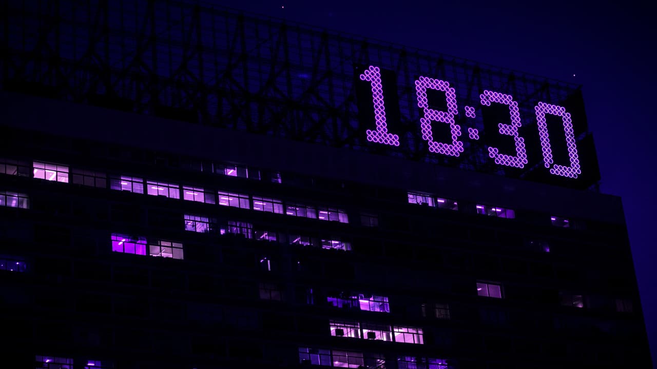 A digital clock reading 18:30 lit up in purple neon on the side of a city building at night