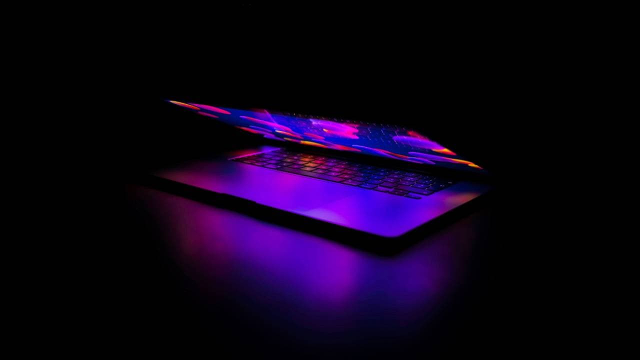 An open laptop glowing with colourful abstract light against a black background