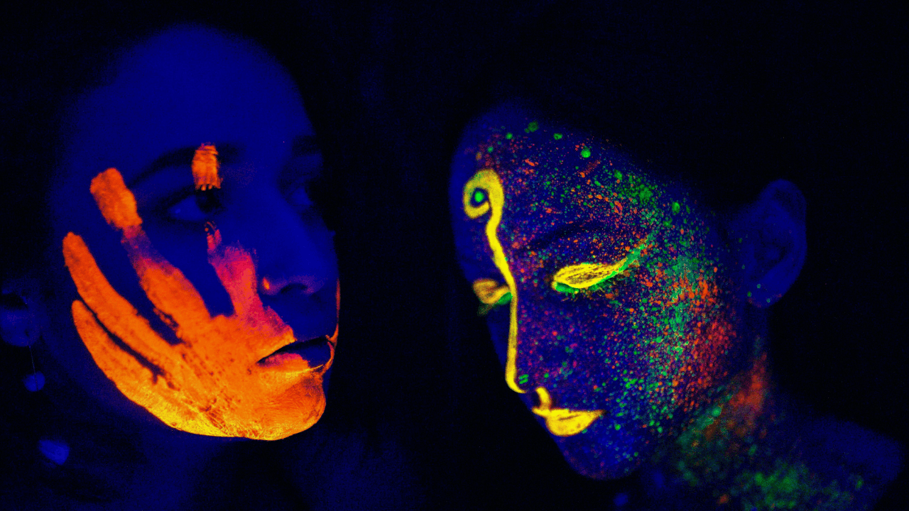 Close-up portrait of a person with vivid blue, yellow, and orange neon body paint against a black background