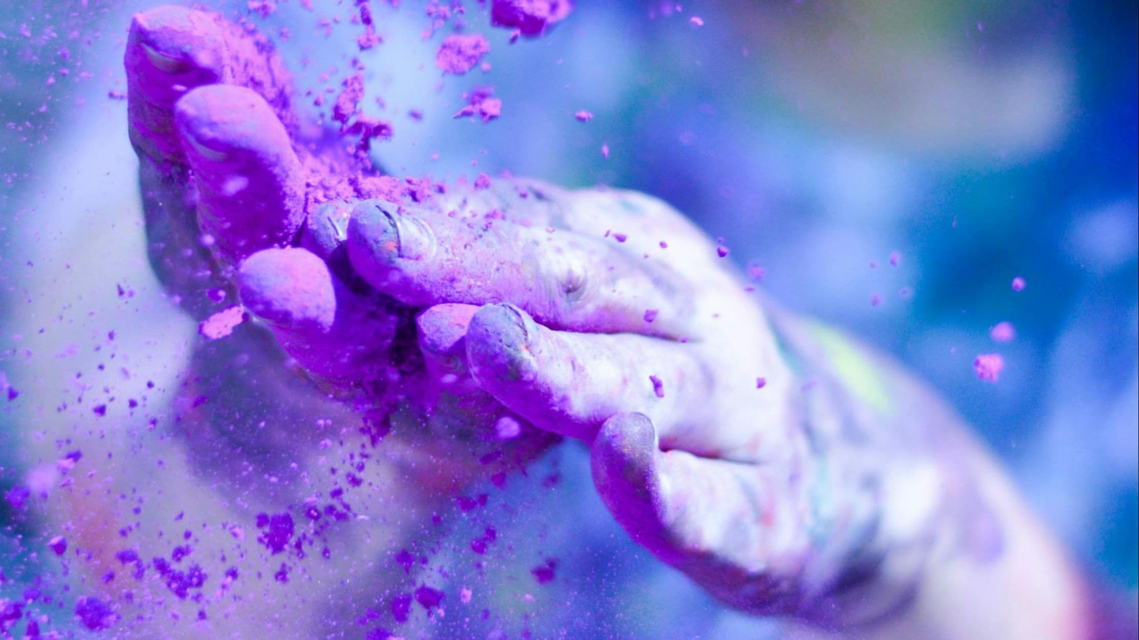 Close-up of purple powder exploding from a hand against a blue background, evoking vibrant human energy