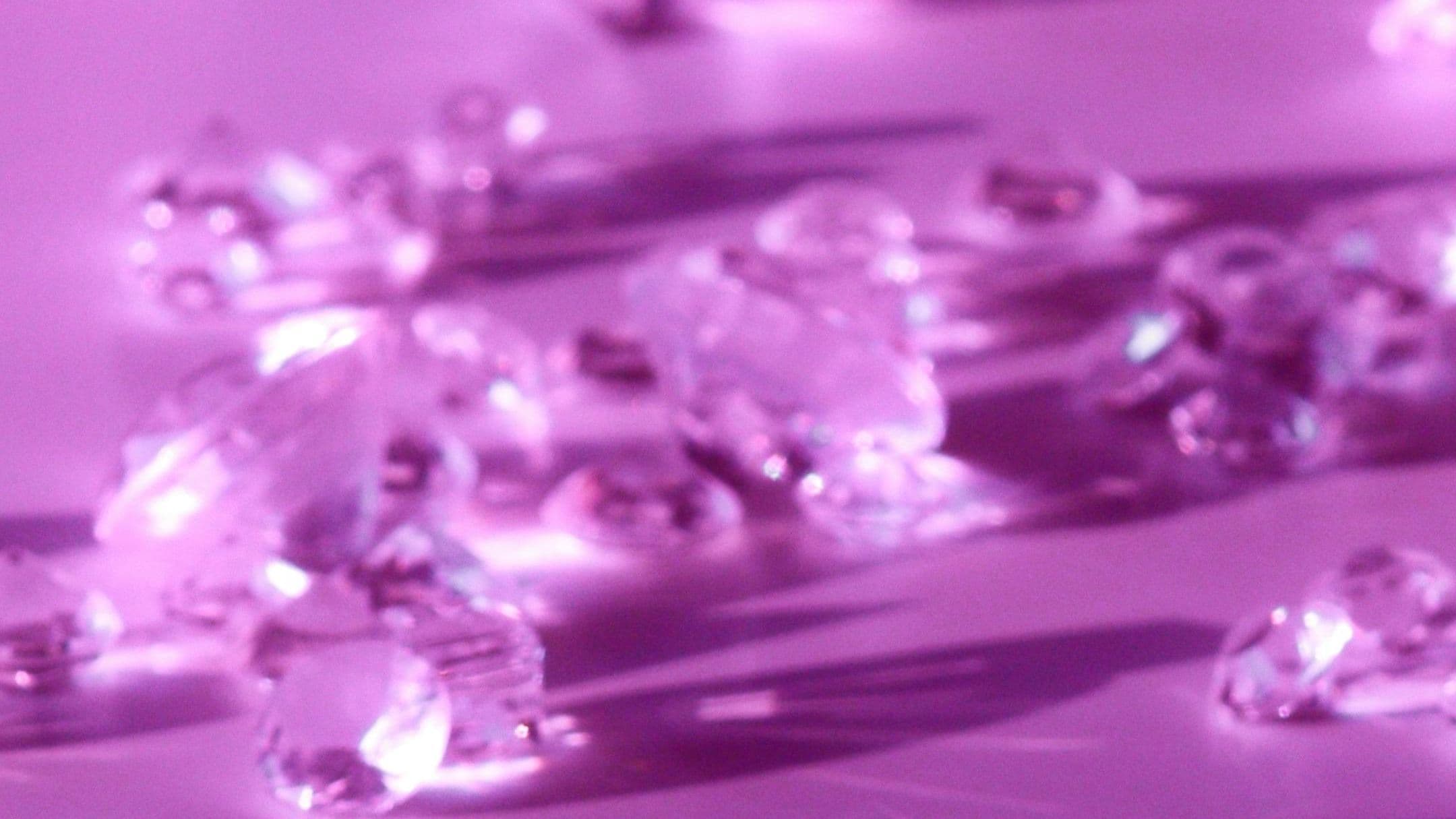 Close-up of scattered diamonds catching light against a pink and purple background
