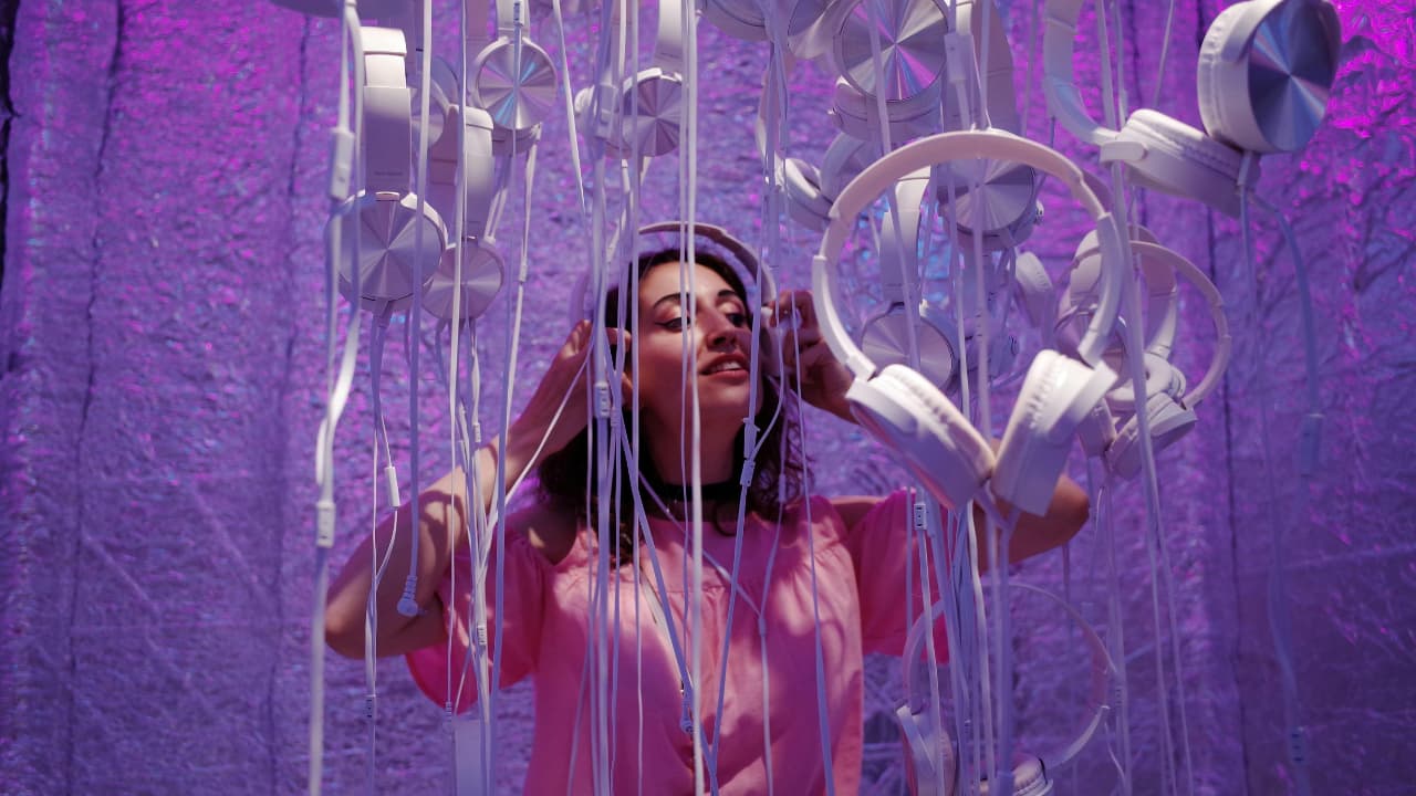 Rows of white headphones hanging by their cables against a purple textured backdrop