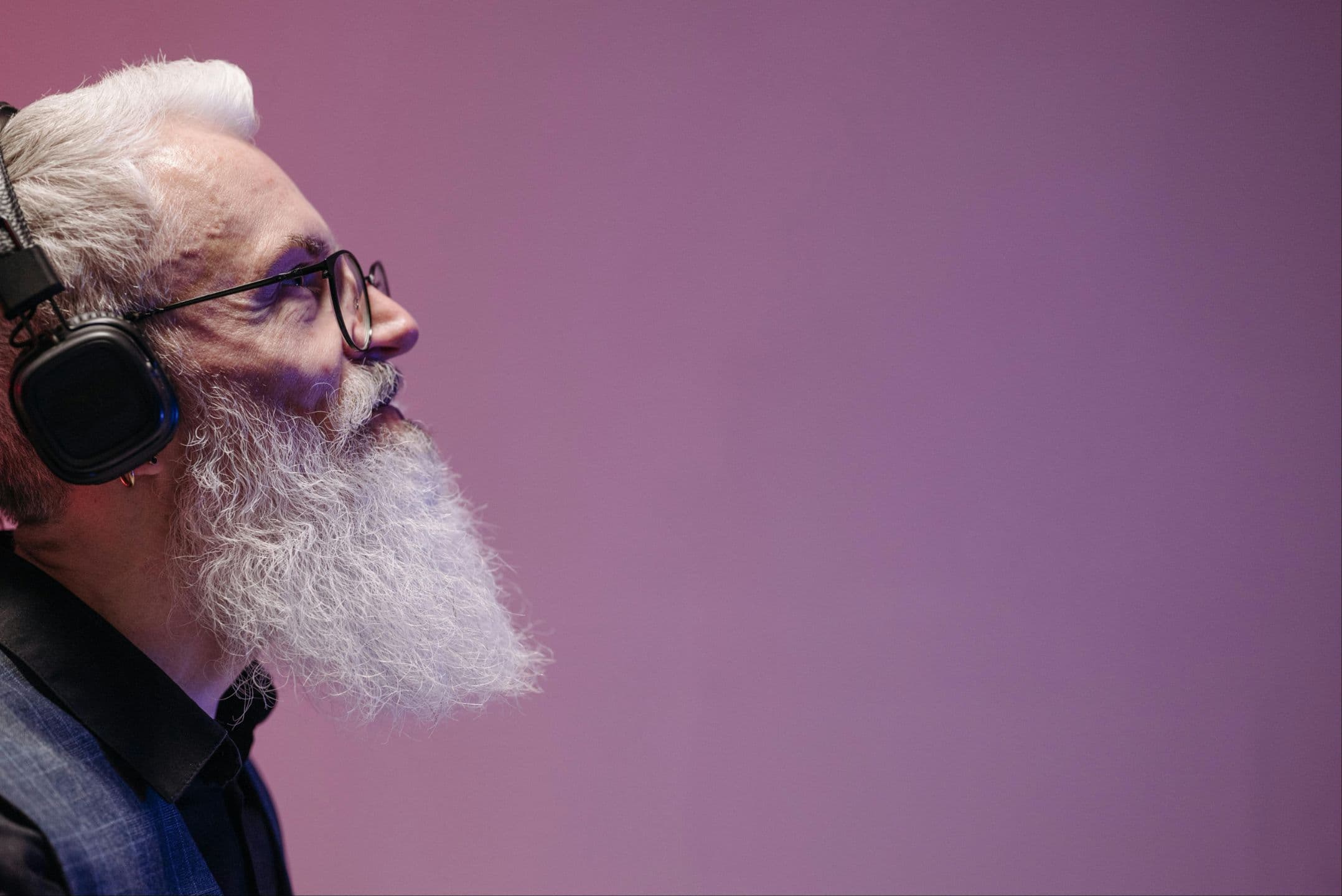 A grey-bearded man wearing headphones, listening intently