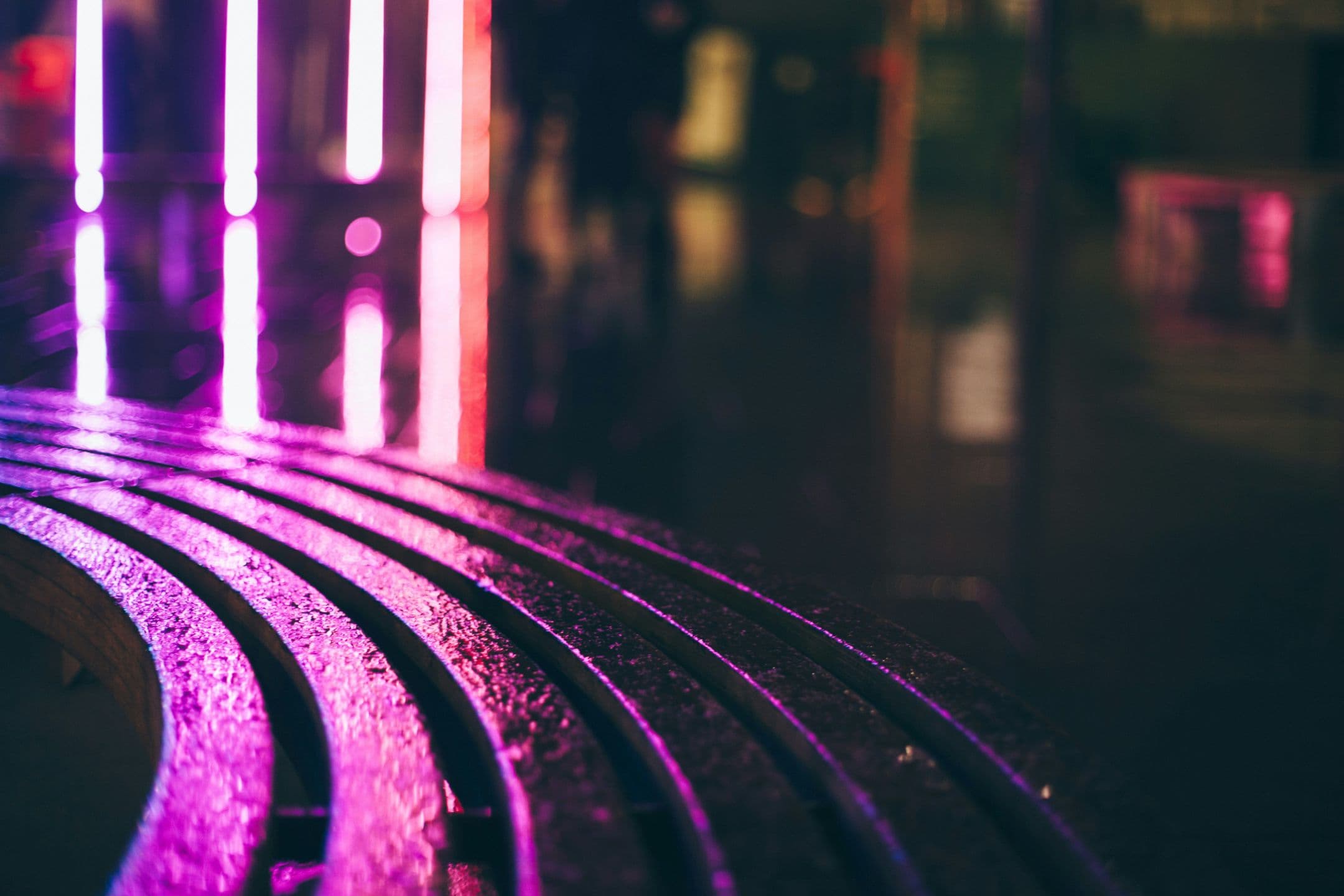 Neon purple lights reflecting on curved city street furniture at night
